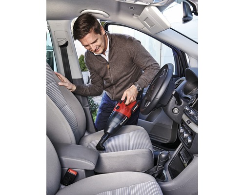 Man dammsuger insidan av en bil med en sladdlös handdammsugare. Dammsugaren är röd och svart.