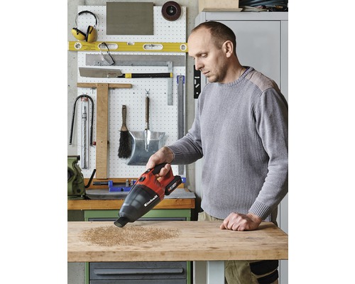 Man dammsuger träflisor från en arbetsbänk med en Einhell sladdlös handdammsugare.