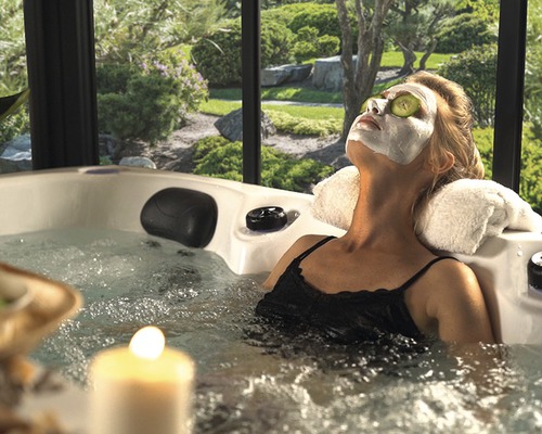 Kvinna som kopplar av med ansiktsmask och gurkskivor i en bubbelpool i trädgården.