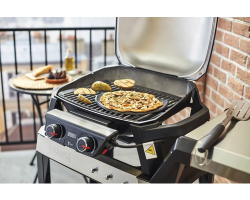 Weber grill med mat på grillgallret och på ett bord i bakgrunden