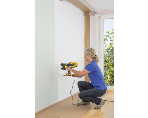 Kvinna använder färgspraysystem för innerväggar.