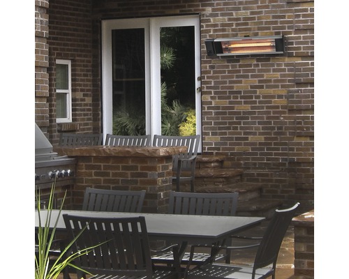 Uteplats med infraröd värmare på tegelvägg ovanför trädgårdsbord och stolar.