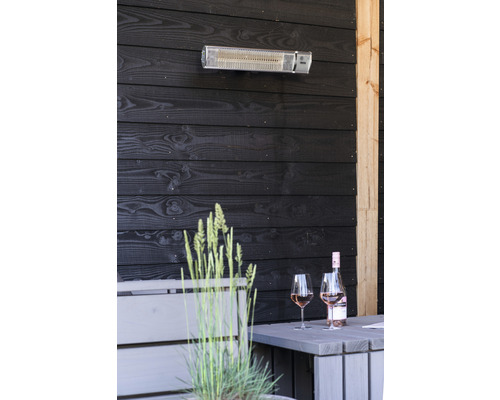 Terrass med värmelampa, bord, vinflaska och glas framför mörk träpanel