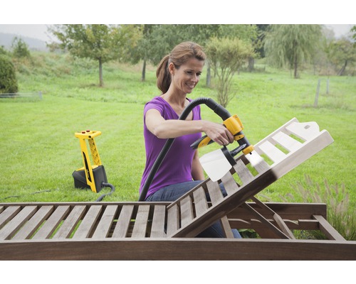 Kvinna använder färgspraysystem för att måla en solstol i trä i trädgården.