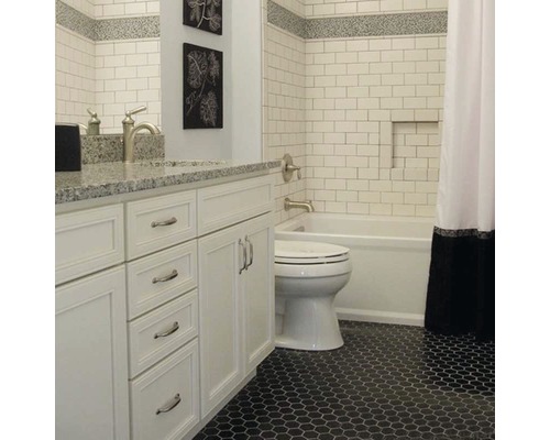 Badrum med vita kakelplattor, tvättställ och svart mosaikgolv.