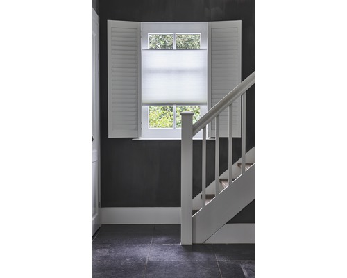 Interiörscen med fönster, fönsterluckor, plisségardiner och trappa.