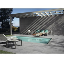 Terrass med pool, klinkergolv, väggbeklädnad och sittgrupp under en pergola.