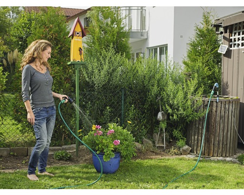 Kvinna vattnar blommor med en trädgårdsslang i trädgården.