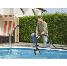 En man använder en dränkbar pump för att tömma en pool i trädgården.