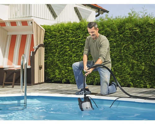 En man använder en dränkbar pump för att tömma en pool i trädgården.