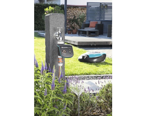 Scen med en kran, en Gardena bevattningsdator, en grässpridare och en robotgräsklippare i trädgården.