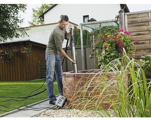 En man installerar en sänkbar pump i en trädgårdsbrunn.