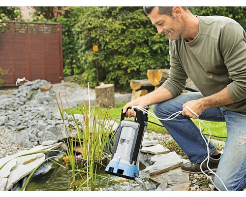 Man använder en dammpump vid trädgårdsdammen.