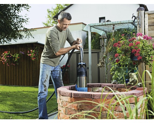 Man som använder en manuell kolvpump vid brunnen i trädgården.