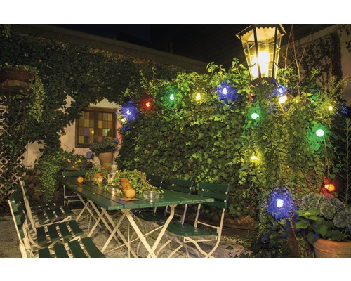 Uteplats med gröna trädgårdsmöbler, upplyst med en ljusslinga och en lykta.