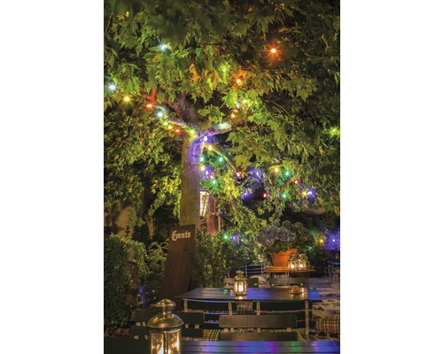 Upplyst trädgård med bord, stolar och lyktor under ett träd med ljusslingor.