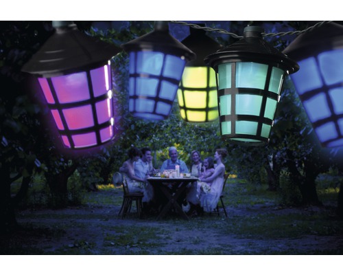 Ljusslinga med färgglada lyktor över en familj som sitter i trädgården