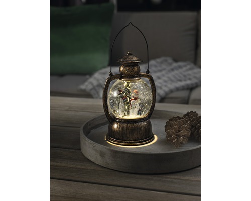 Dekorativ snöglobslykta med snögubbe och julgran på en bricka