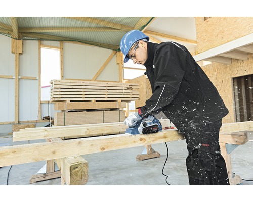 En hantverkare hyvlar en träplanka med en elektrisk hyvel i en verkstad.