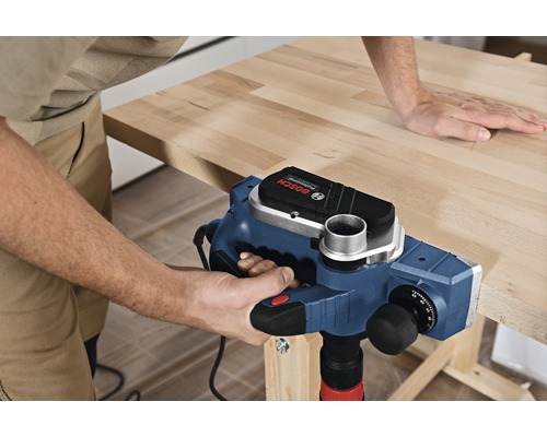 Hantverkare bearbetar ett arbetsstycke med en elektrisk hyvel. Bosch Logo.