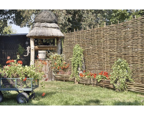 Scen med trädgårdsbrunn, pilstaket, blomstervagn och planterade pilkorgar