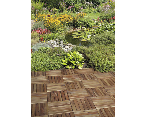 Lagt träplattmönster i en trädgård med damm och blomsterrabatter