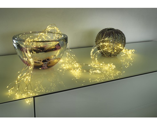 Dekorativ ljusslinga draperad runt en glasskål och en klotformad vas på en möbel.