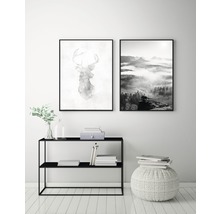 Två inramade bilder med ett hjortmotiv och en landskapsvy ovanför en svart hylla och en vit pall