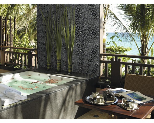 Badrum med mosaikvägg, badkar och bord på en terrass med havsutsikt