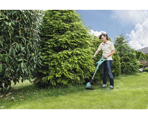 Kvinna använder grästrimmer i trädgården.