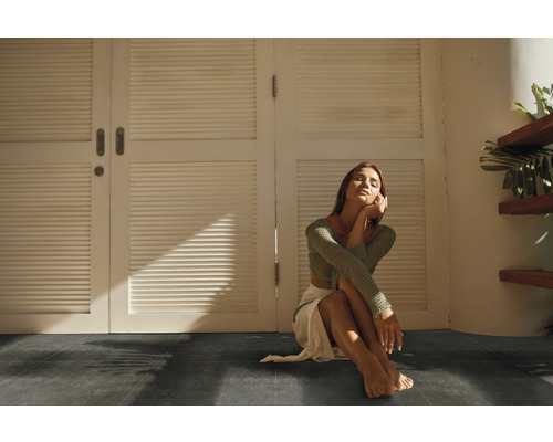 Interiör med mörkt golv och en kvinna som sitter framför en vit dörr