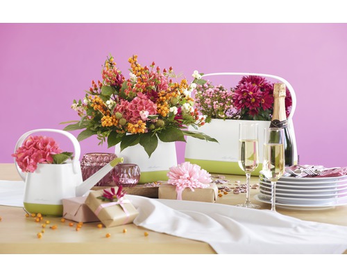Dekorativt bord med blomsterarrangemang i ytterkrukor, presenter, champagne och porslin