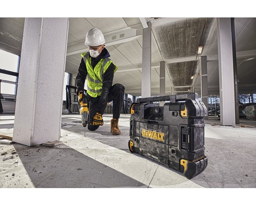 En byggnadsarbetare borrar med en borrmaskin i en byggnad, bredvid honom en Dewalt-laddare.