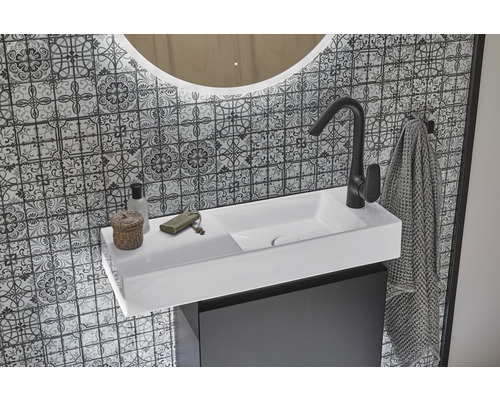 Tvättställ med blandare, handduk och spegel framför mönstrad vägg