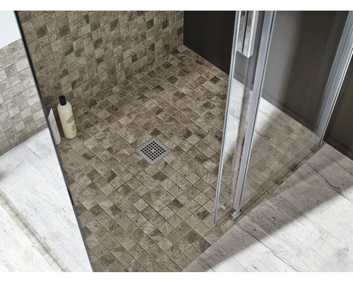 Detaljvy av en dusch med mosaikplattor, duschkabin och avlopp