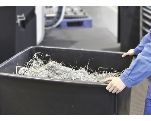 En person håller ett svart tråg fyllt med metallspån.