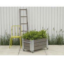 Rullbar planteringslåda i trä med metallförstärkningar, gul stol och stege framför vitt staket