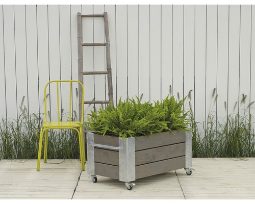 Rullbar planteringslåda i trä med metallförstärkningar, gul stol och stege framför vitt staket