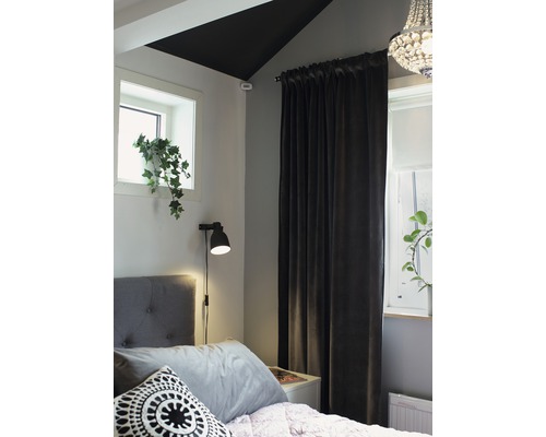 Sovrum med säng, gardiner, lampa och fönster med växt.