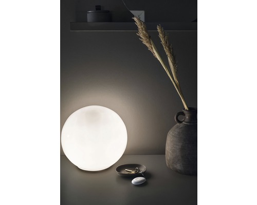 Dekorativ bordslampa med sfärisk form bredvid vas och nycklar