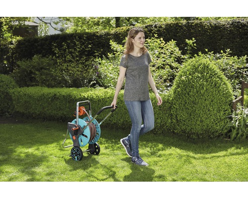 Kvinna drar en trädgårdsslangvagn på en gräsmatta.