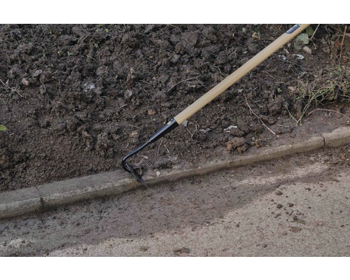 Trädgårdshacka med trähandtag i bruk bredvid en trottoarkant