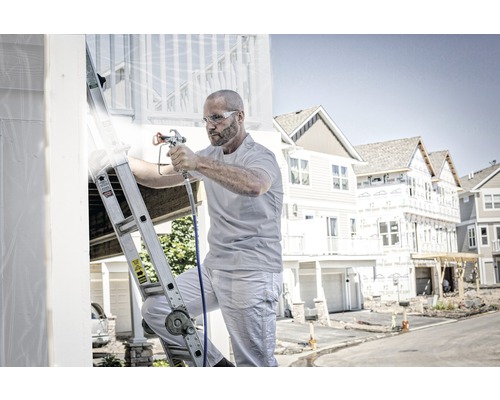 Man på stege som målar ett hus med en färgspruta