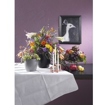 Arrangemang med blommor, frukt, ljus och en inramad bild av en vit påfågel på ett bord