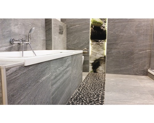 Badrum med badkar, gråa kakelplattor och stenstrandgolv