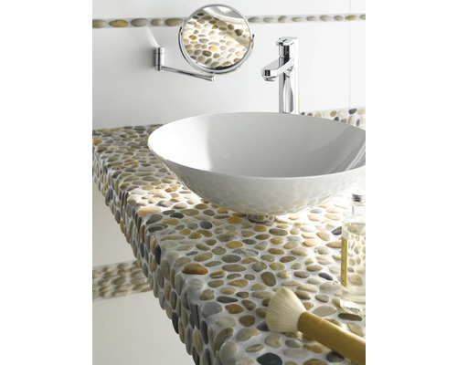 Badrumsscen med tvättställsskål, armatur, väggspegel och en hylla med småsten