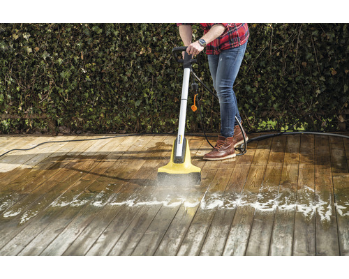 En person rengör en träterrass med en elektrisk terrassrengörare.