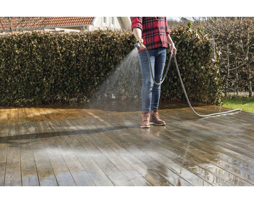 En person rengör en träterrass med en vattenslang.