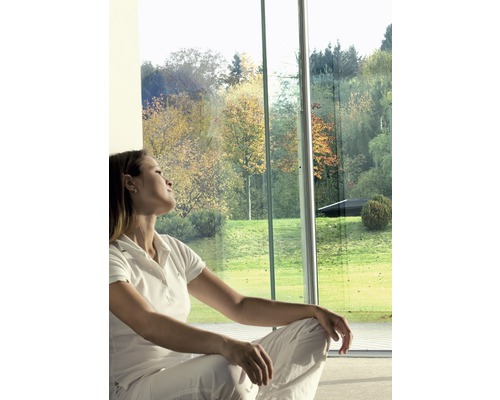 Kvinna sitter framför ett stort fönster med utsikt över en trädgård