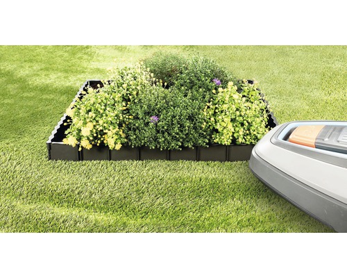 Rabattkant av plast med växter och robotgräsklippare i trädgården.